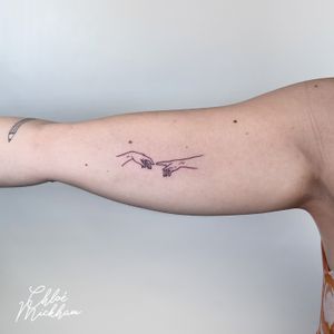 Fine line tattoo by Chloe Mickham featuring dainty hands symbolizing the act of creation.