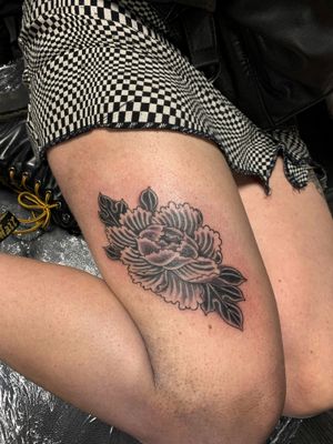 Elegant upper leg tattoo featuring a detailed black and gray peony flower, done by artist Alex Travers.
