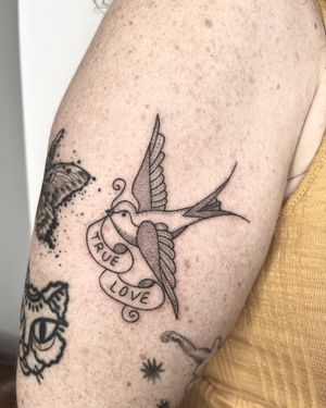 Get a unique handpoke tattoo on your upper arm by Indigo Forever Tattoos featuring a small traditional bird motif and inspiring quote.