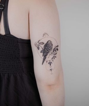 Elegant micro-realism tattoo on upper arm featuring a bird within a circle by El Bernardes.