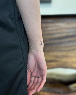 Get a small lettering forearm tattoo of your special date in roman numerals by renowned artist Hana Kaki.