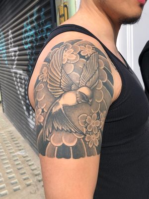 Elegant black and gray tattoo by Carlos Zucato featuring a beautiful combination of a bird and flower motif on the upper arm.