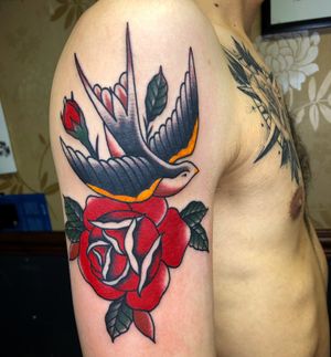 Beautiful upper arm tattoo featuring a traditional style bird and flower motif, impeccably executed by Carlos Zucato.