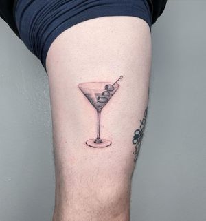 Get a taste of sophistication with this micro-realism cocktail tattoo featuring a martini glass and olives. By artist Martin Rosenberg.