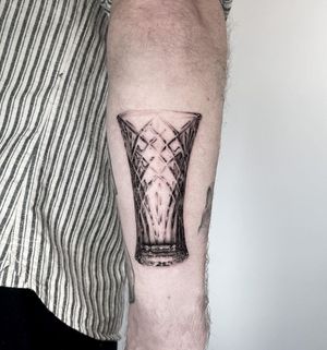 Stunning micro realism tattoo of a crystal glass on the lower arm by Martin Rosenberg. Detailed and lifelike design.