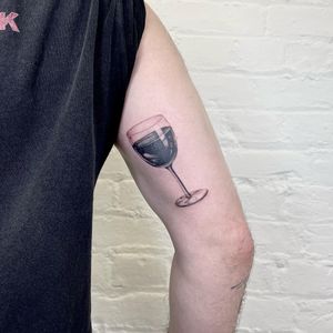 Fine line black and gray tattoo of a realistic wine glass by artist Martin Rosenberg on upper arm.