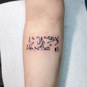 George Antony's small lettering tattoo on forearm featuring a quote and coordinates.