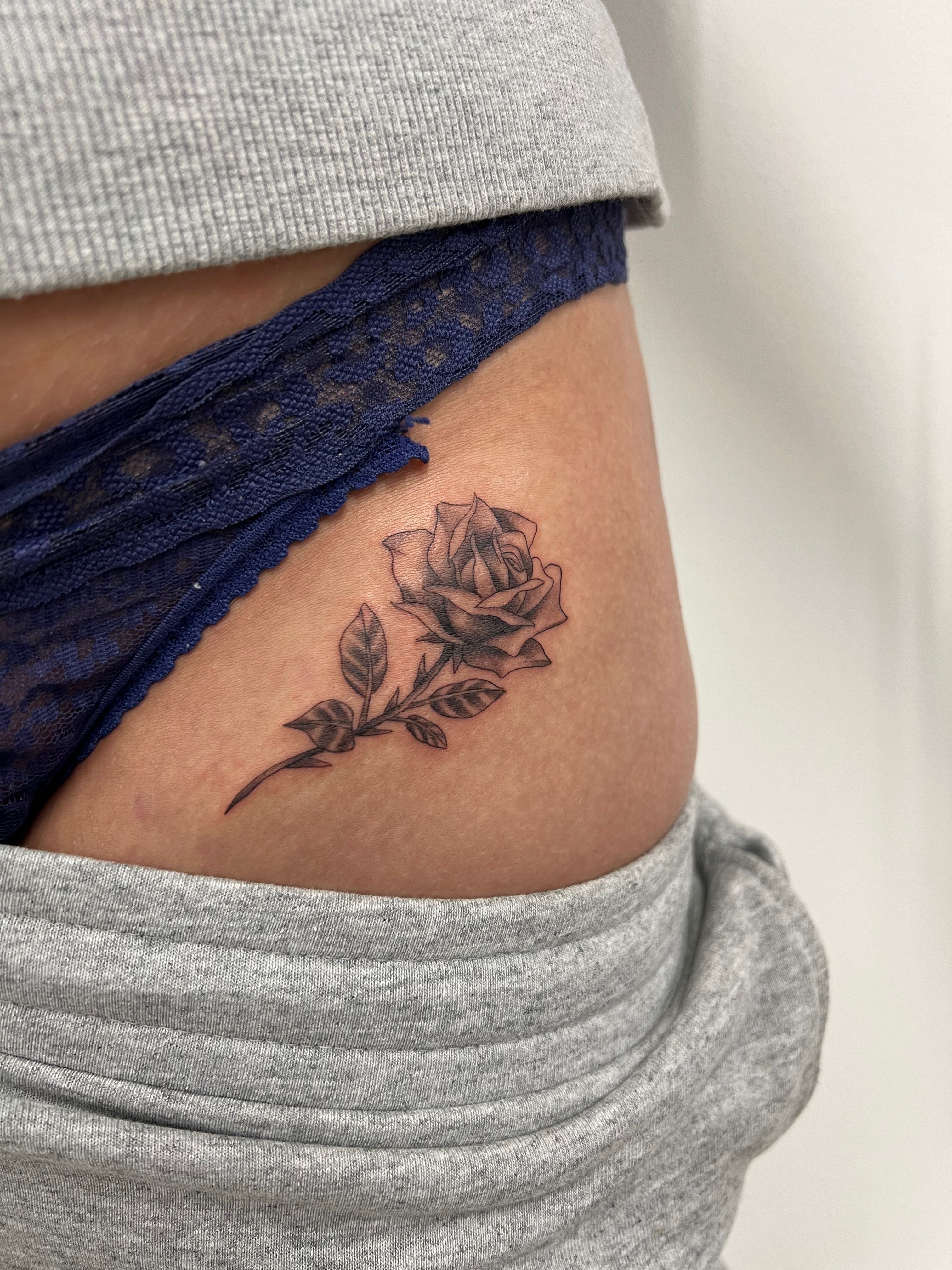 Dark rose tattoo on lower rib and hip