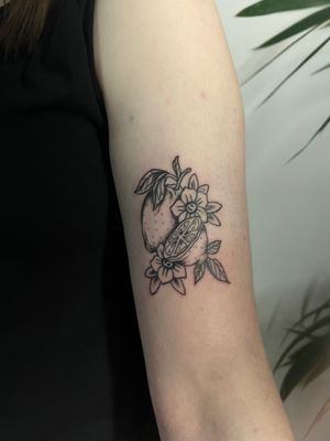 Get a stylish black and gray tattoo of a realistic orange on your upper arm by tattoo artist Kayleigh Cole. Perfect for fruit lovers!