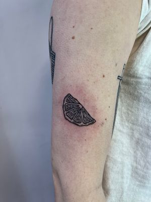 Sleek and detailed orange fruit tattoo on upper arm, expertly crafted by Kayleigh Cole.