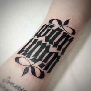 Unique lettering tattoo by Chun Lee featuring a meaningful quote with intricate pattern details on the arm.