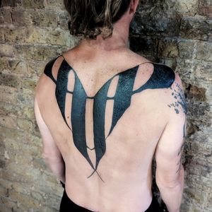 Experience the artistry of Chun Lee with this mesmerizing blackwork tribal pattern tattoo on your upper back.
