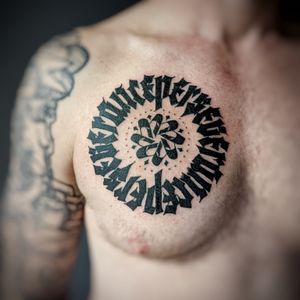 Blackwork chest tattoo by Chun Lee featuring a unique pattern and meaningful quote in bold lettering.