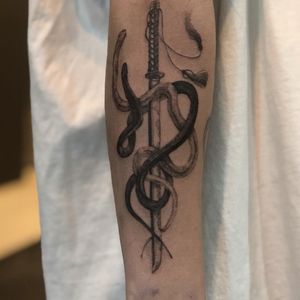 Embrace the power and mystery with this stunning black and gray tattoo by Hansol Jung, featuring a striking snake coiled around a menacing dagger.