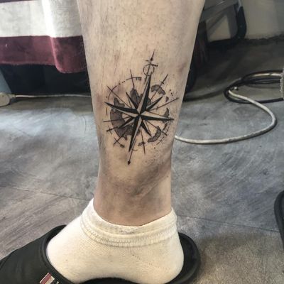 Explore new horizons with this blackwork lower leg tattoo featuring a sleek compass and intricate map design by Hansol Jung.