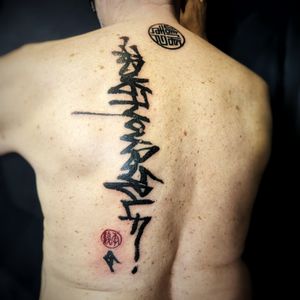 Masterfully executed calligraphy by Chun Lee, make a bold statement with this impactful blackwork lettering tattoo on your back.
