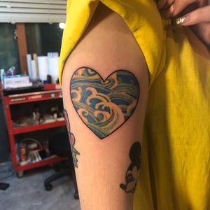 Get a vibrant new school tattoo on your upper arm featuring a heart and waves, expertly done by Hansol Jung.
