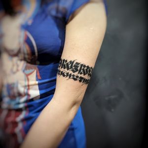 Get a stylish lettering tattoo on your upper arm with a unique pattern and inspiring quote by tattoo artist Chun Lee.