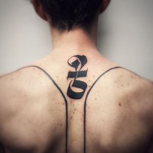Bold blackwork lettering intertwines in a stunning pattern design on the upper back, expertly done by artist Chun Lee.