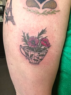 Adorn your upper arm with a fine line tattoo featuring a charming teacup and intricate flowers, created by the talented artist Kiky Flore.