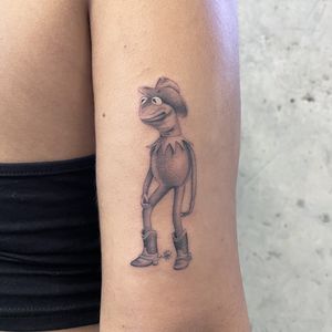 Get a unique black and gray cowboy frog tattoo on your upper arm by Fresh Flower. Embrace your inner cowboy with this stylish design.