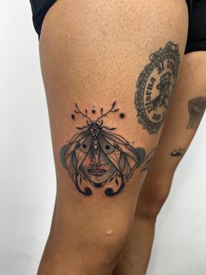 Elegant neo-traditional fine line tattoo featuring a beautiful moth and face design on the upper leg. Created by talented artist Kiky Flore.