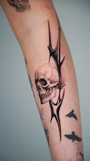Bold blackwork design by Jacky Yang featuring a skull motif intertwined with intricate tribal patterns on the forearm.