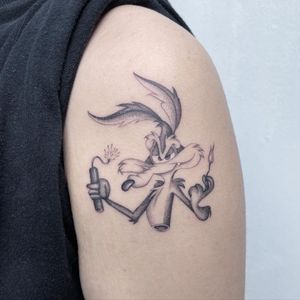 Capture the dynamic energy of a coyote surrounded by dynamite in this striking black and gray anime tattoo on your upper arm. By Fresh Flower.