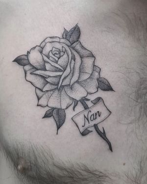 Display a beautiful black & gray flower tattoo with a personalized name on your arm, created by talented artist Elisa Thirteen.