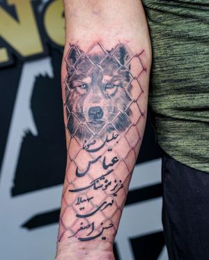 Stunning black and gray forearm tattoo featuring a detailed wolf, fence, and piercing eyes. By Soheyl Astangi.