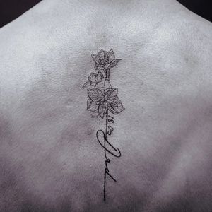 Fine line small lettering tattoo on upper back by Soheyl Astangi featuring a delicate flower and meaningful quote.