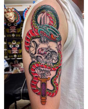 Intricately designed upper arm tattoo by Alex Travers featuring a powerful combination of a snake, skull, and sword in traditional Japanese style.