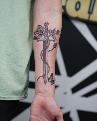 A powerful combination of a black and gray traditional style tattoo featuring a beautiful rose intertwined with a sharp sword. Designed by the talented artist Soheyl Astangi.