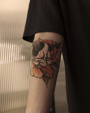 Vibrant neo-traditional tattoo by Jacky Yang featuring a beautiful flower and fierce hannya mask on lower arm.
