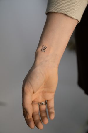 Elegant number tattoo by Federico Tronconi in small lettering style on the wrist.
