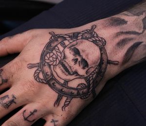 Classic black and gray design featuring a skull with a steering wheel and rope, expertly done by José on the hand.