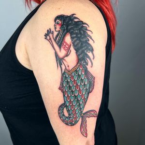 Get a stunning traditional mermaid tattoo on your upper arm by the talented artist Claudia Trash, featuring a native motif.