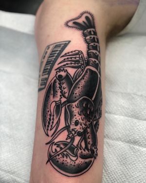 Experience the intricate beauty of a black and gray lobster tattoo expertly inked on your upper arm by tattoo artist Claudia Trash.
