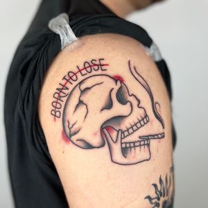 Unique black and gray fine line tattoo on upper arm by Claudia Trash. Skull with smoking quote lettering design.