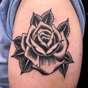 Stunning upper arm tattoo by Claudia Trash, featuring a beautiful black & gray traditional flower design.
