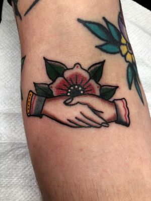A beautiful traditional tattoo featuring a detailed hand and flower design on the forearm by artist Claudia Trash.