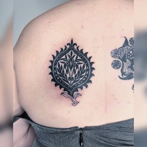 Elegant ornamental design with intricate leaf motif created by tattoo artist Kiky Flore for a stunning upper back tattoo.