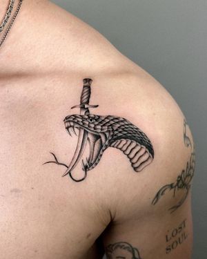 Incredible black and gray shoulder tattoo of a striking snake and dagger by Joshua Williams. Unleash your inner warrior.