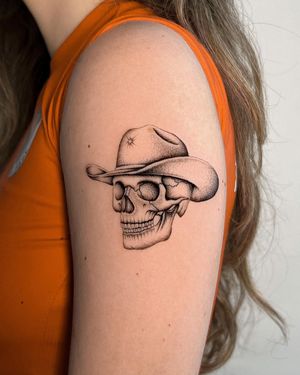 Get a striking black and gray tattoo of a skull wearing a hat on your upper arm by Joshua Williams. Perfect for those who love edgy designs.
