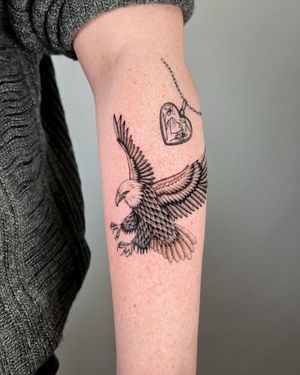 Unleash your inner strength with this powerful blackwork tattoo by Joshua Williams, featuring a fierce eagle, delicate heart, and intricate pendant design.