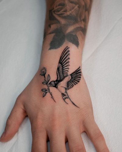 Elegant black and gray design by Joshua Williams, combining a beautiful bird and intricate floral elements on the hand.