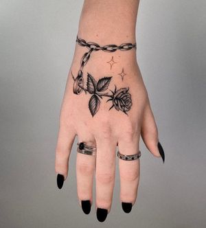 Black & gray fine line micro realism hand tattoo featuring a detailed rose intertwined with a chain, by Joshua Williams.