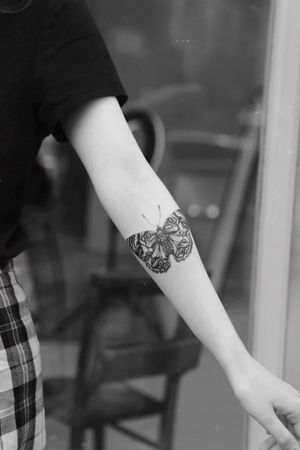 Stunning black moth tattoo adorning the forearm, created with intricate blackwork technique by the talented artist Jamie B.
