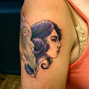 Adorn your upper arm with a stunning new school tattoo featuring a feather and a woman, done in beautiful purple ink by artist Frankie Brown.