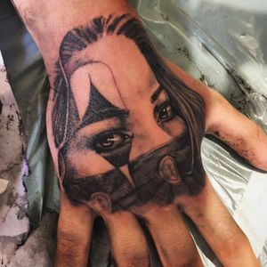 Get a stunning black and gray tattoo of a woman and clown on your hand by the talented artist Frankie Brown.